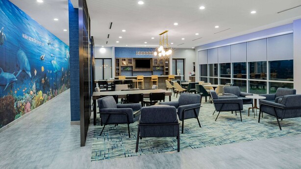 A modern lounge area with seating, a bar, and a large mural of an underwater scene. - La Quinta Inn & Suites by Wyndham Galveston North at I-45 (Galveston)