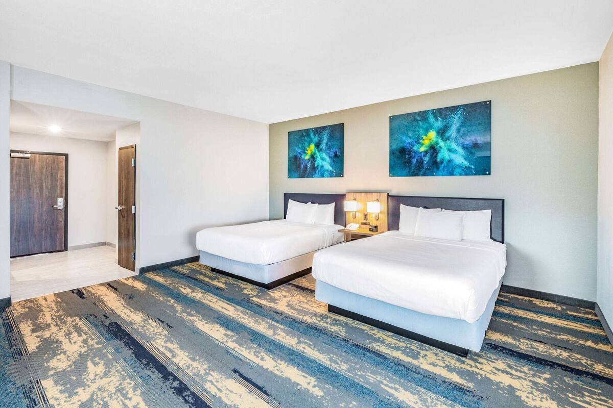 Une chambre d’hôtel avec deux lits, une grande fenêtre et des œuvres d’art abstraites accrochées au mur.