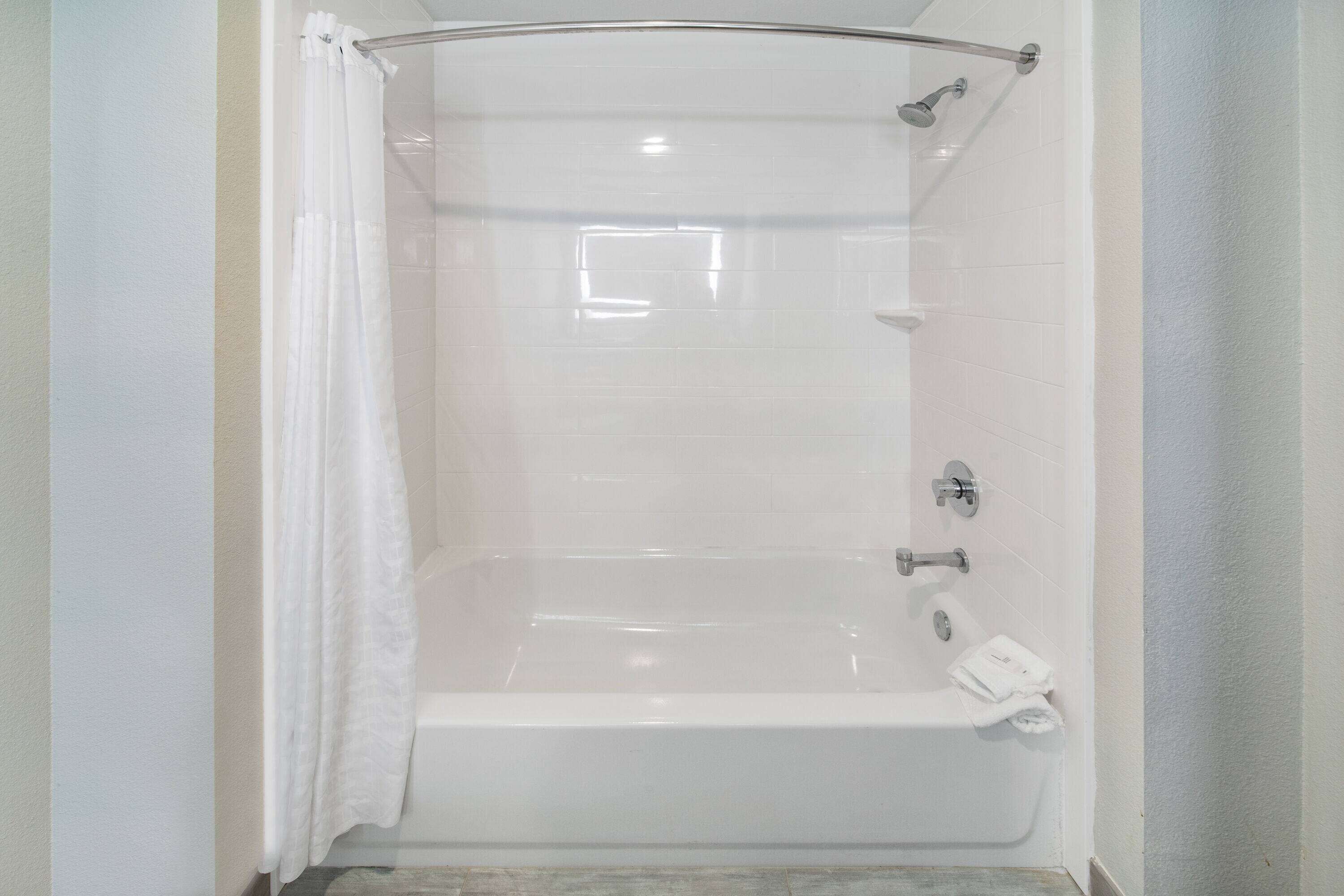 Una cabina de ducha con paredes de vidrio transparente, una cortina blanca, un cabezal de ducha manual y un perchero para toallas.