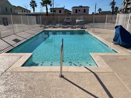 A rectangular swimming pool with a metal safety railing, surrounded by a white fence.