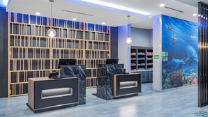 A modern reception area with marble reception desks, a wooden wall with vertical slats, and an aquarium wall. - La Quinta Inn & Suites by Wyndham Galveston North at I-45 (Galveston)
