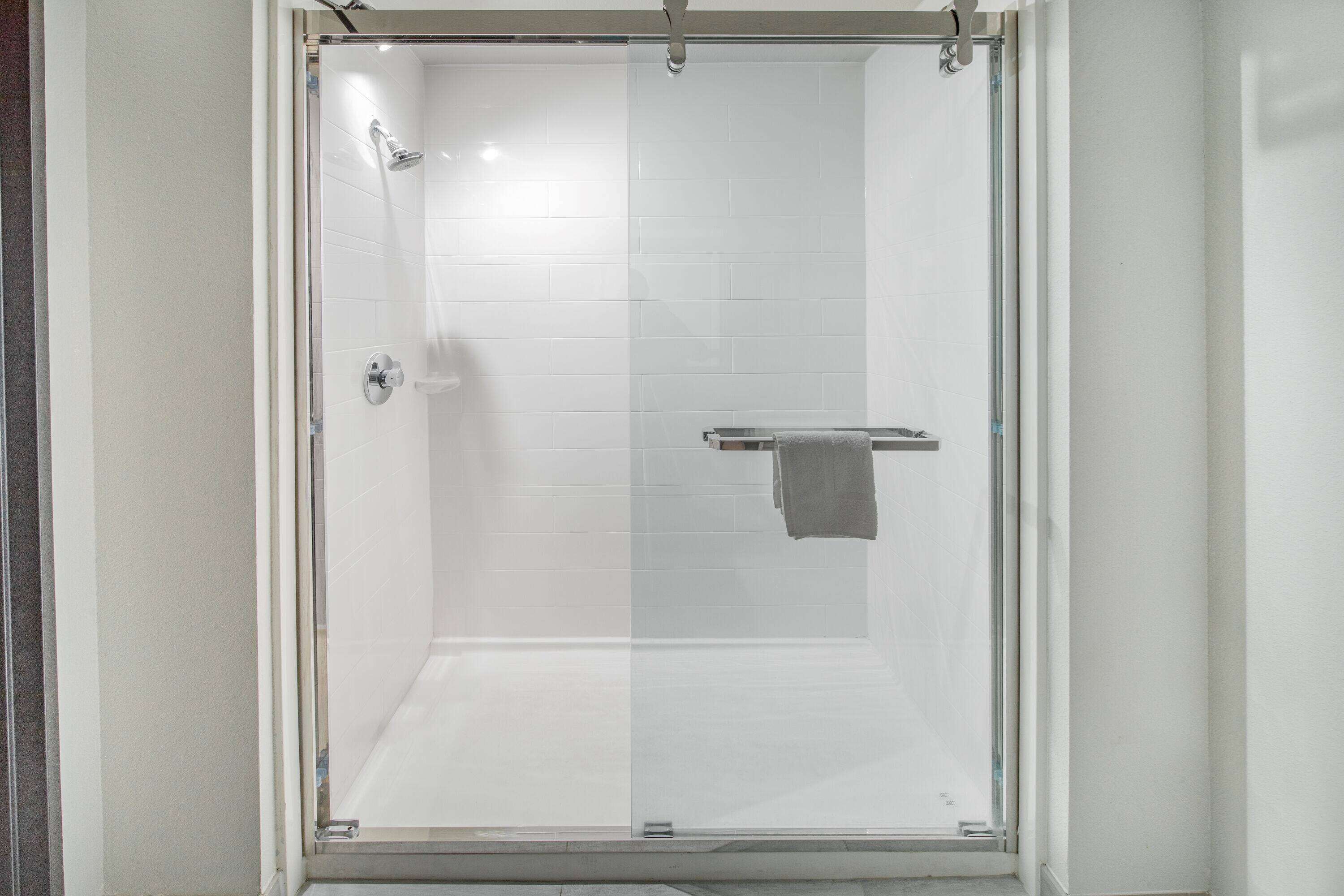 A glass-enclosed shower with a white tiled wall and a towel rack.