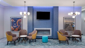 A lobby with a flat-screen TV mounted on the wall, a fireplace, and four armchairs with a round table in the center. - La Quinta Inn & Suites by Wyndham Galveston North at I-45 (Galveston)