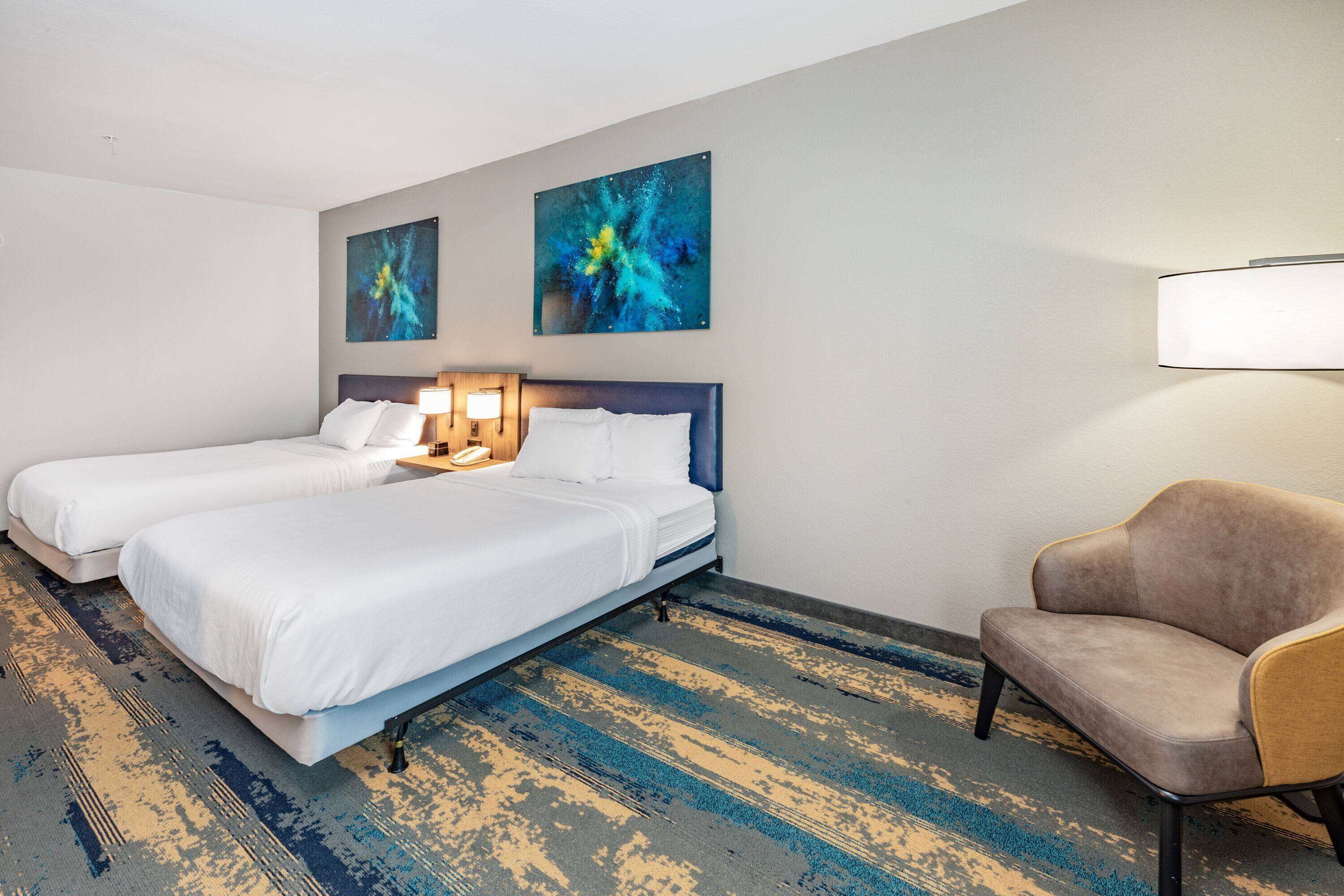 A hotel room with two beds, a sofa, and abstract wall art.