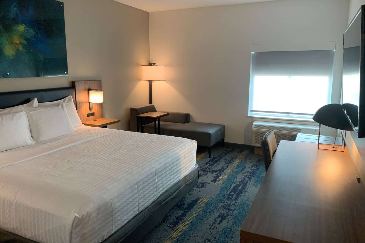 Une chambre d’hôtel avec un grand lit, un bureau, une chaise, une lampe et une fenêtre.