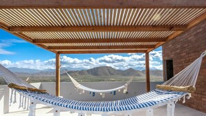 A hammock under a wooden pergola on a rooftop terrace with a view of mountains.