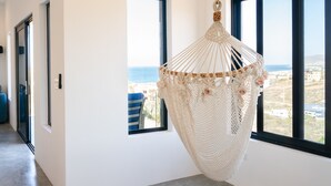 A modern interior with a macramé hanging chair, large windows, and a view of the sea.