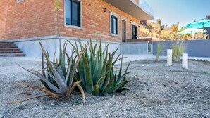 A modern building with a brick facade, a balcony, and a garden with aloe plants.
