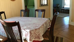 Ein Essbereich mit einem mit Spitze bedeckten Tisch, umgeben von Holzsesseln, einer grünen Wand und einer Tür zu einem weiteren Raum.