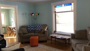 Ein Wohnzimmer mit blauer Wand, einem braunen Sofa, einem Holztisch und einem kleinen orangefarbenen Hocker.
