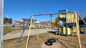 Children can play on the playground's slide and swing set in a grassy field.