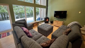 Ein gemütliches Wohnzimmer mit großen Fenstern, einem Kamin und einem Flachbildfernseher.