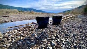 Zwei Campingstühle am steinigen Flussufer, im Hintergrund ein Berg.