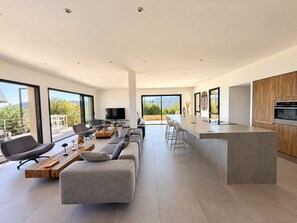 A modern kitchen with a large island, bar stools, and a dining area with a sofa and chairs.
