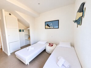 A hotel room with two single beds, a small seating area, a wardrobe, and a wall-mounted artwork.