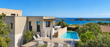 A modern villa with a swimming pool, outdoor seating, and a view of the sea.
