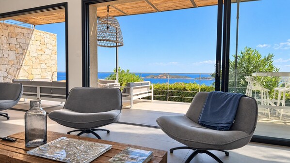 A modern outdoor seating area with a stone wall, a hanging light fixture, and a view of the sea.