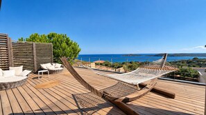 A wooden deck with a hammock, white wicker chairs, and a view of the sea. - Villa Mela di Pinarello (Conca)