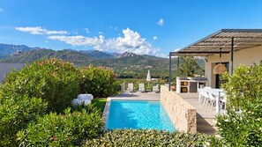 A pool area with a view of mountains, outdoor seating, and a pergola.