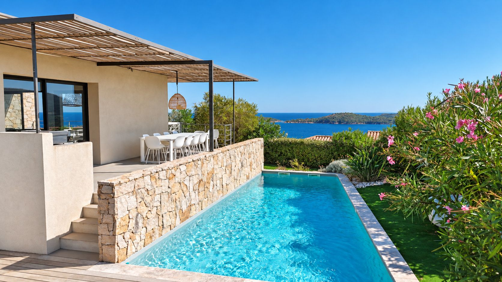 A swimming pool with a stone wall, a covered patio with outdoor furniture, and a view of the sea.