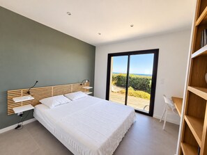 A bedroom with a bed, bedside tables, a desk, and a view of the outdoors. - Villa Mela di Pinarello (Conca)