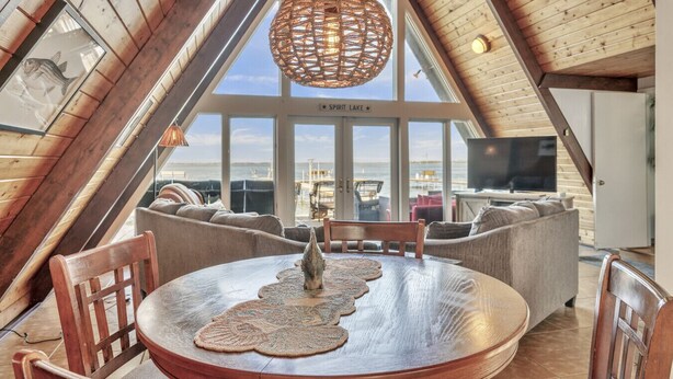Una habitación acogedora con techos altos y un amplio ventanal con vistas al Lago Spirit, que incluye una mesa redonda de madera con un mantel tejido, una lámpara colgante de fibras naturales y una zona de estar confortable.
