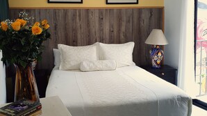 A bedroom with a bed, a nightstand, a lamp, a vase with flowers, and a window with a view.