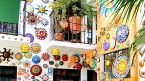 A courtyard with a green tiled floor, a blue bench, and a variety of colorful sun-shaped decorations on the walls.