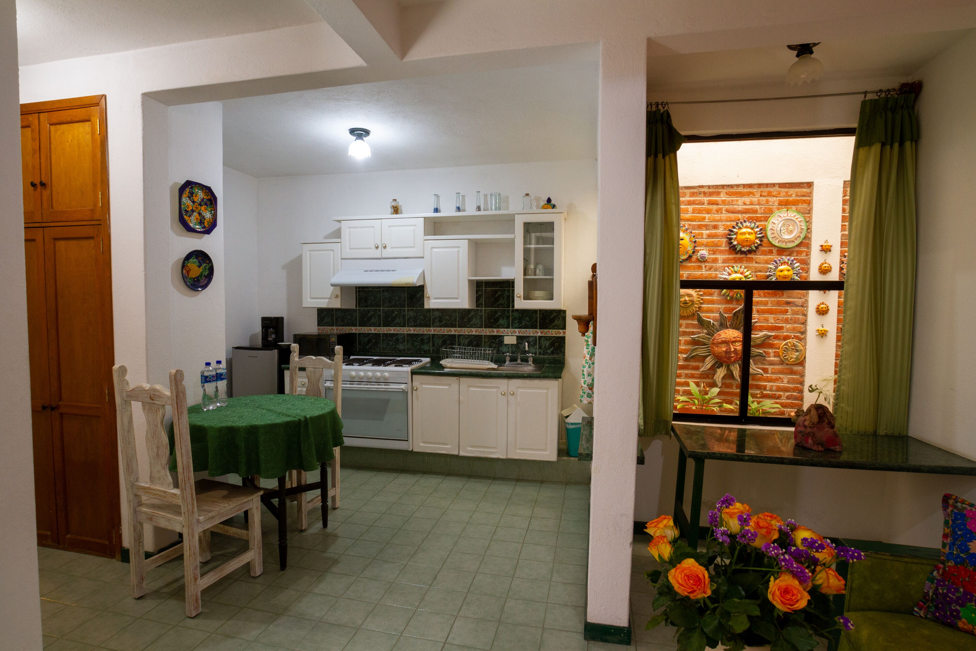 Cocina compacta con muebles blancos, estufa y mesa de comedor con sillas.
