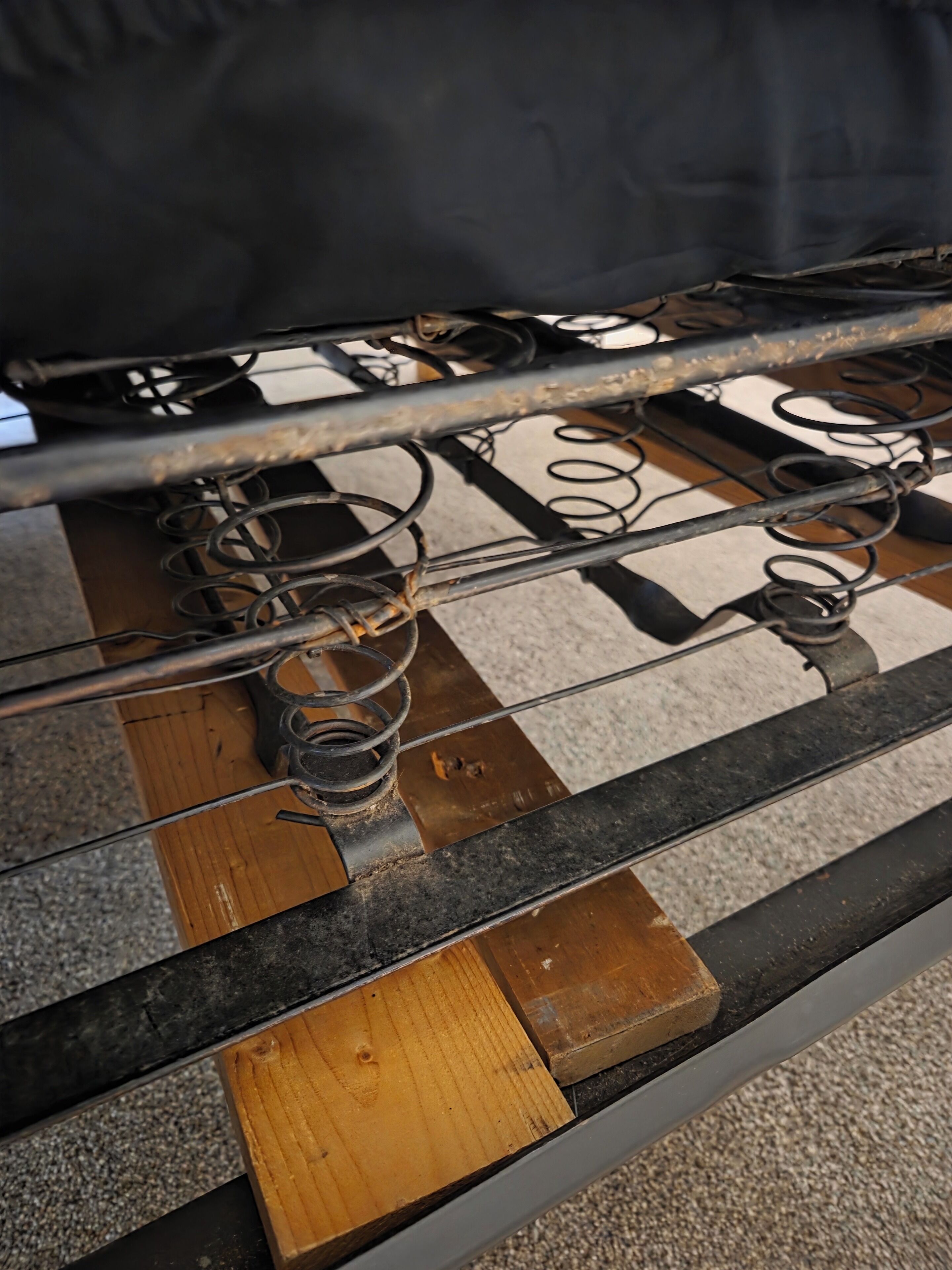 A close-up of a bed frame with metal springs and wooden panels.
