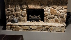 Una chimenea de piedra con un cartel con la letra 'G' encima, un tronco de leña y una bolsa de plástico en la repisa.