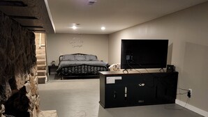 Una sala de estar moderna con una pared de acento de piedra, un televisor de pantalla plana grande, un sofá y una cama con ropa de cama estampada.