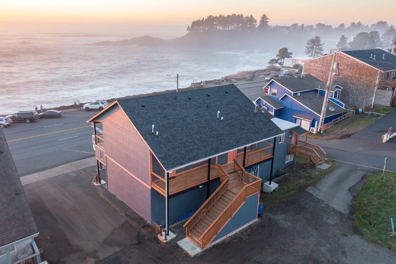 A coastal building with a wooden deck and a staircase leading to a second floor.