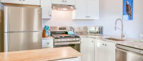 A modern kitchen with white cabinets, stainless steel appliances, and a wooden countertop.