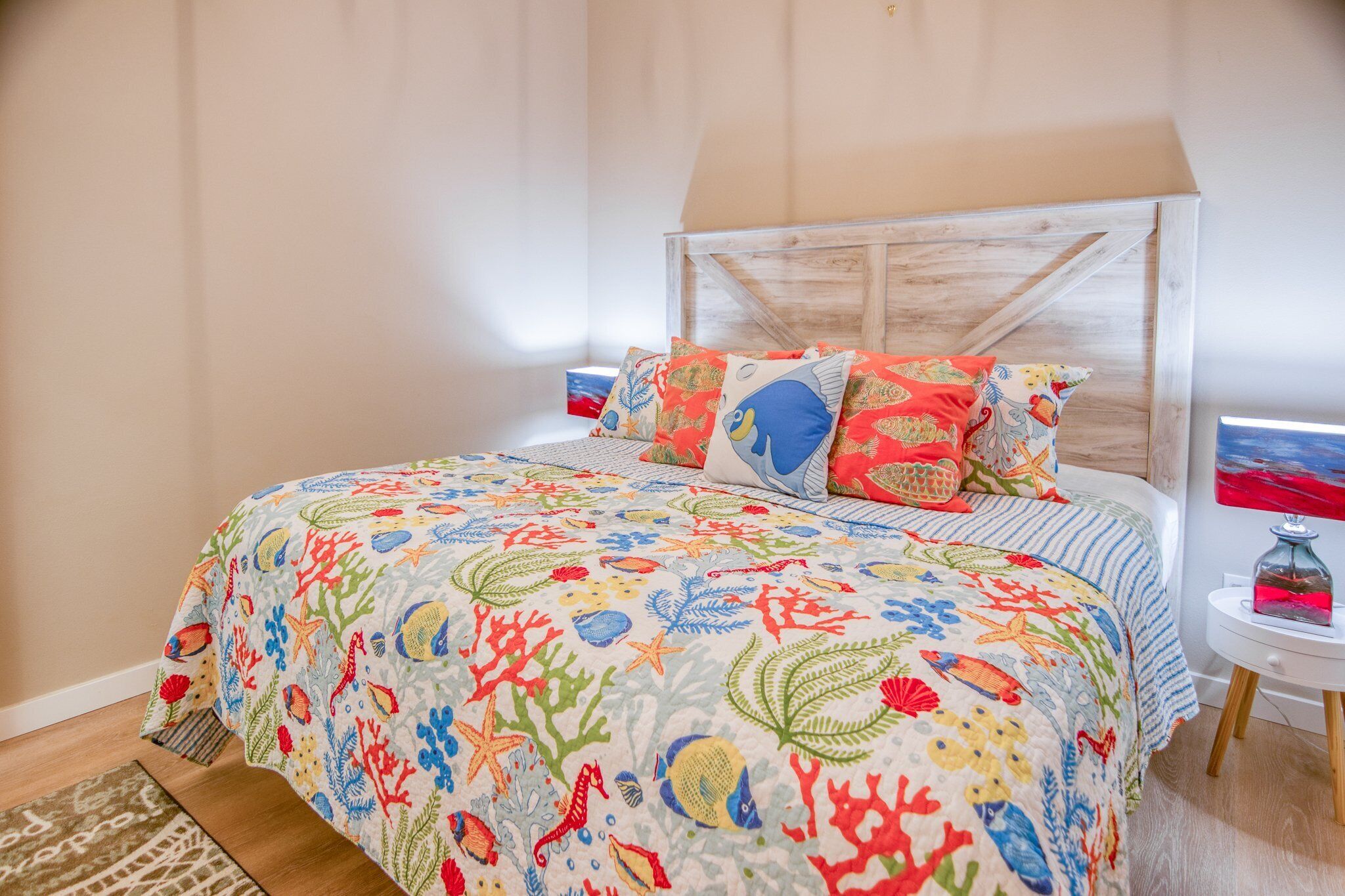A bed with a colorful coral-themed bedspread, a wooden headboard, and a small bedside table with a lamp.