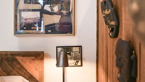 A bedroom with a wooden headboard, a framed collage on the wall, a lamp, a vintage telephone, and antler decorations. - Suite 4: Outpost · Gorgeous Farm Carriage House Loft (Berryville)