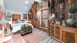 A room with a bed, wooden wall decor, a globe, and a cabinet with carvings. - Suite 4: Outpost · Gorgeous Farm Carriage House Loft (Berryville)