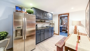 A modern kitchen with a stainless steel refrigerator, dark cabinets, and a wooden dining table. - Suite 4: Outpost · Gorgeous Farm Carriage House Loft (Berryville)