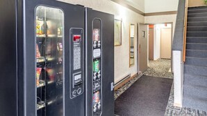 A vending machine area with multiple machines, a carpeted floor, and a staircase leading to another floor. - Motel6 Fond Du Lac, WI (Fond du Lac)