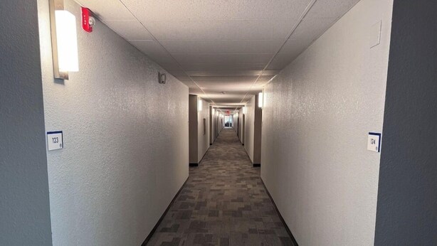 A long, narrow hotel corridor with carpeted floors and walls marked with room numbers. - Motel6 Fond Du Lac, WI (Fond du Lac)
