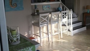Uma área de refeições com mesa e cadeiras brancas, um ventilador de teto e uma escada que sobe.