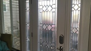 Uma porta branca com um painel de vidro jateado e uma grade metálica decorativa.