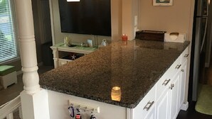 Cozinha com bancada de granito, armários brancos e iluminação pendente.