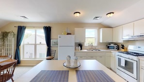 A modern kitchen with white cabinets, a refrigerator, a stove, a microwave, and a sink. There is a dining table with two placemats and two mugs with "CHILI" and "HELLO" on them. - 1 Bdrm Pet friendly Rental/ Walkable to Village (Skaneateles)