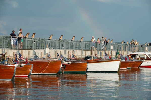 A marina with wooden boats docked, a pedestrian walkway, and a rainbow in the sky.