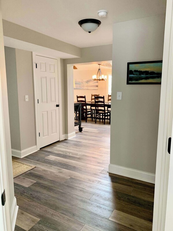 A hallway with a wooden floor, a white door, and a dining area with a table and chairs.
