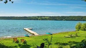 A lakeside view with a dock, boats, and lounge chairs. - Level Lakefront on Owasco Lake! Sleeps 14! (Auburn)