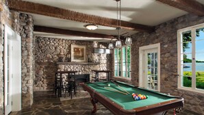 A pool table in a stone-walled room with a fireplace, bar area, and large windows overlooking a lake. - Level Lakefront on Owasco Lake! Sleeps 14! (Auburn)