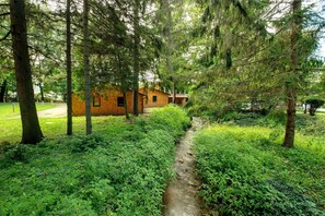 Eine rustikale Holzhütte, umgeben von dichtem Grün und einem schmalen Bach.