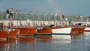 A marina with wooden boats docked, a pedestrian walkway, and a rainbow in the sky.